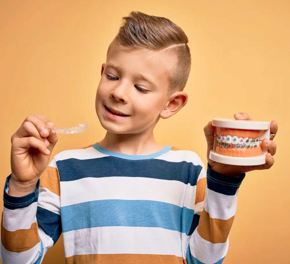 A boy holding a clear aligner and a teeth model