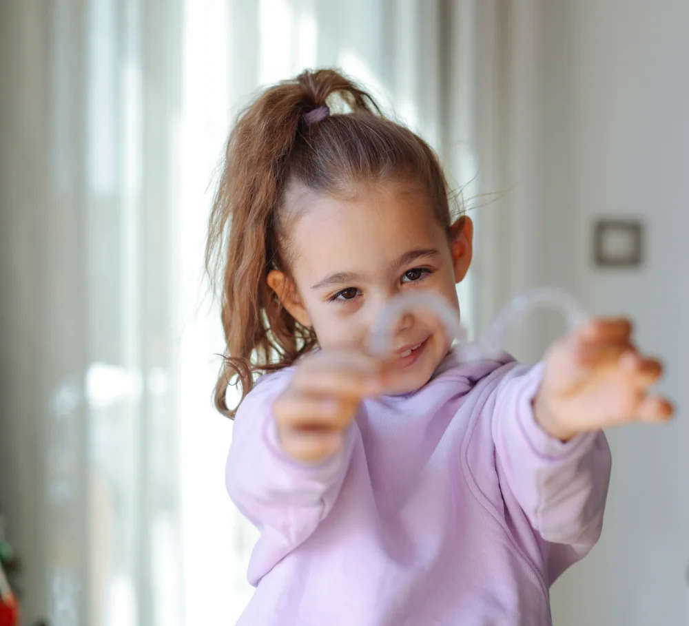 A girl holding out a clear aligner